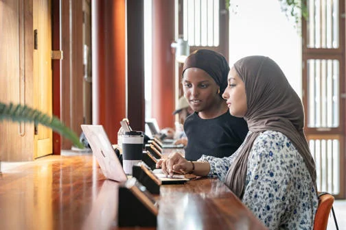 Two students studying together at a library desk.