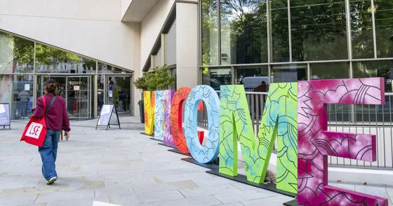 Student with LSE tote bag walking past letters spelling out WELCOME on the LSE campus.