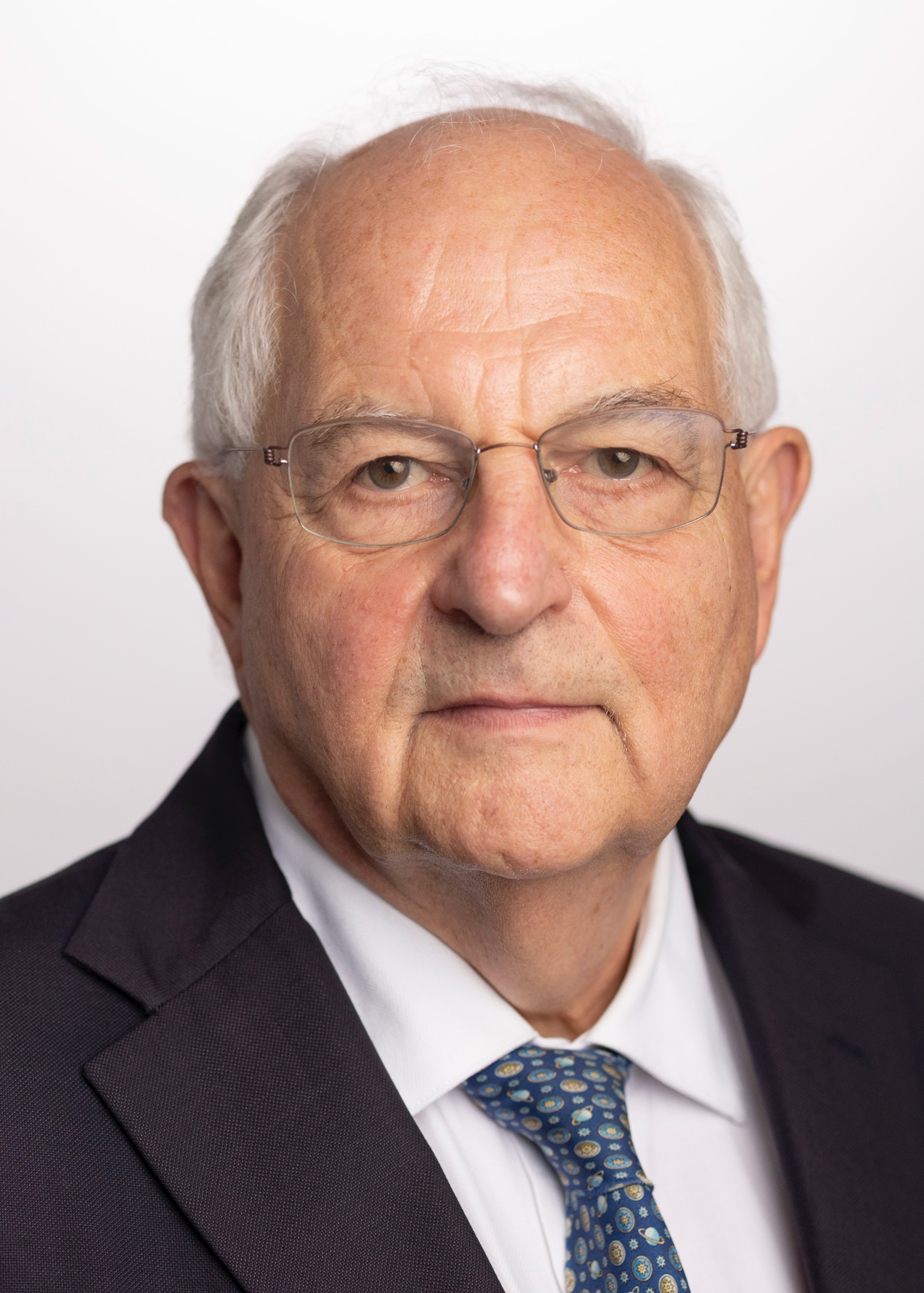 Close up of Martin wearing a suit, blue tie, white shirt and glasses