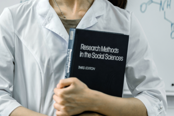 Woman holding book titled 'Research Methods in the Social Sciences'. 