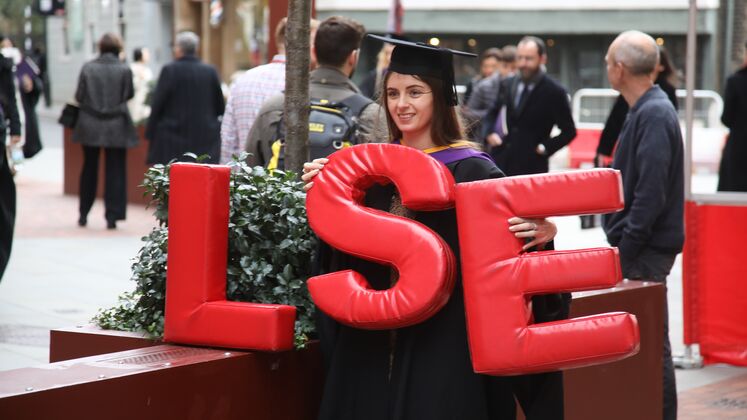 Graduate on LSE campus, holding up 'L', 'S' and 'E' figures.