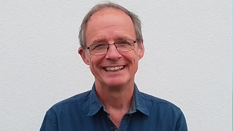 Profile image of Nick Louth showing him wearing a dark blue shirt and standing against a white wall