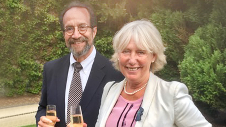 Jeffrey and Rita Golden stand beside each other in a garden both holding a glass of wine