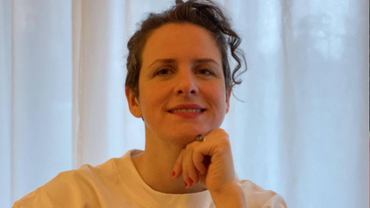 Melissa Knight sits in front of a curtained window with her chin resting on her hand