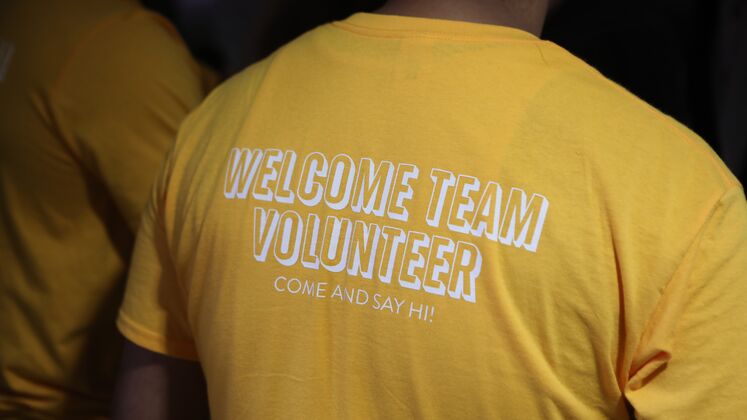 A person wears a yellow t-shirt with the words 'welcome team volunteer' in white letters on their back