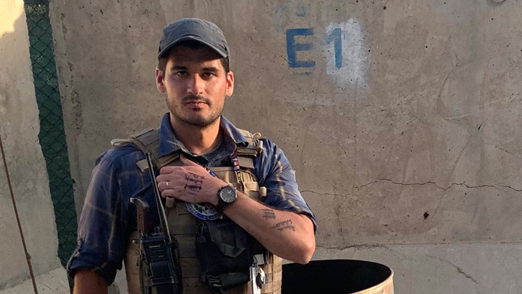 Sam Aronson stands wearing his uniform, including a safety vest, at Kabul Airport. Written on his arm are the names of people he is trying to evacuate.