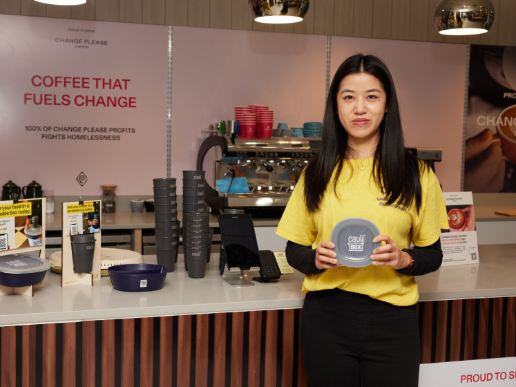 Mingqiao stands in a coffee shop holding a CauliBox container