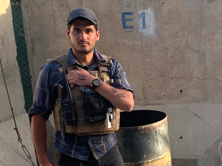 Samuel Aronson stands in front of a wall wearing a security vest in Kabul, Afghanistan