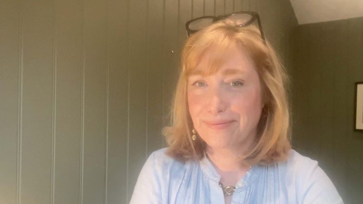 Profile image of Caroline Haynes showing her in a light green painted wooden walled room with a picture behind her