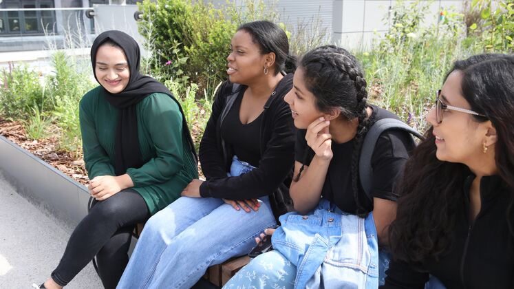 A group of female students laughing and talking while sitting outside on the Centre Building roof terrace