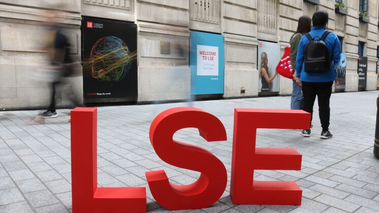 Large red letters spelling LSE sit on Houghton Street. Students can be seen milling about behind them.