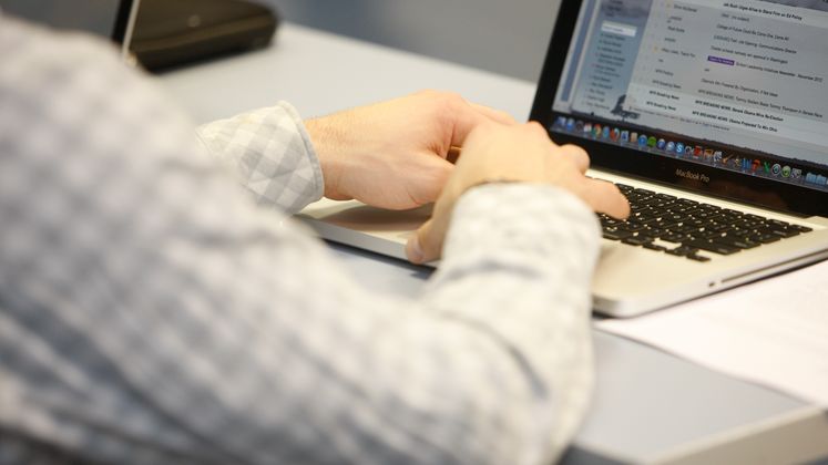 A person in a check shirt types on a laptop