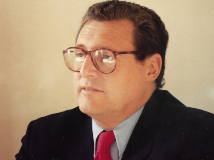 John Gardiner in the 1980s wearing a black suit and a red tie
