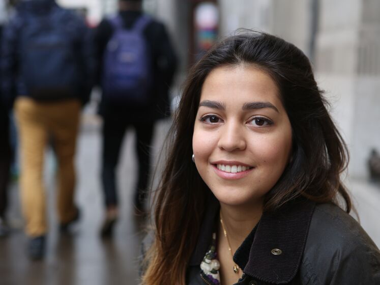 A woman looks at the camera while people with backpacks walk away in the background