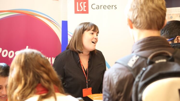 A woman talks to people at the LSE Careers stand at an event