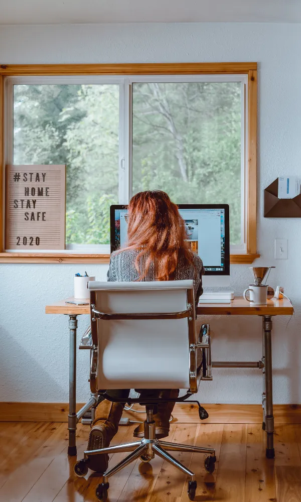 A woman sitting working from a laptop next to a 'stay home stay safe 2020' sign