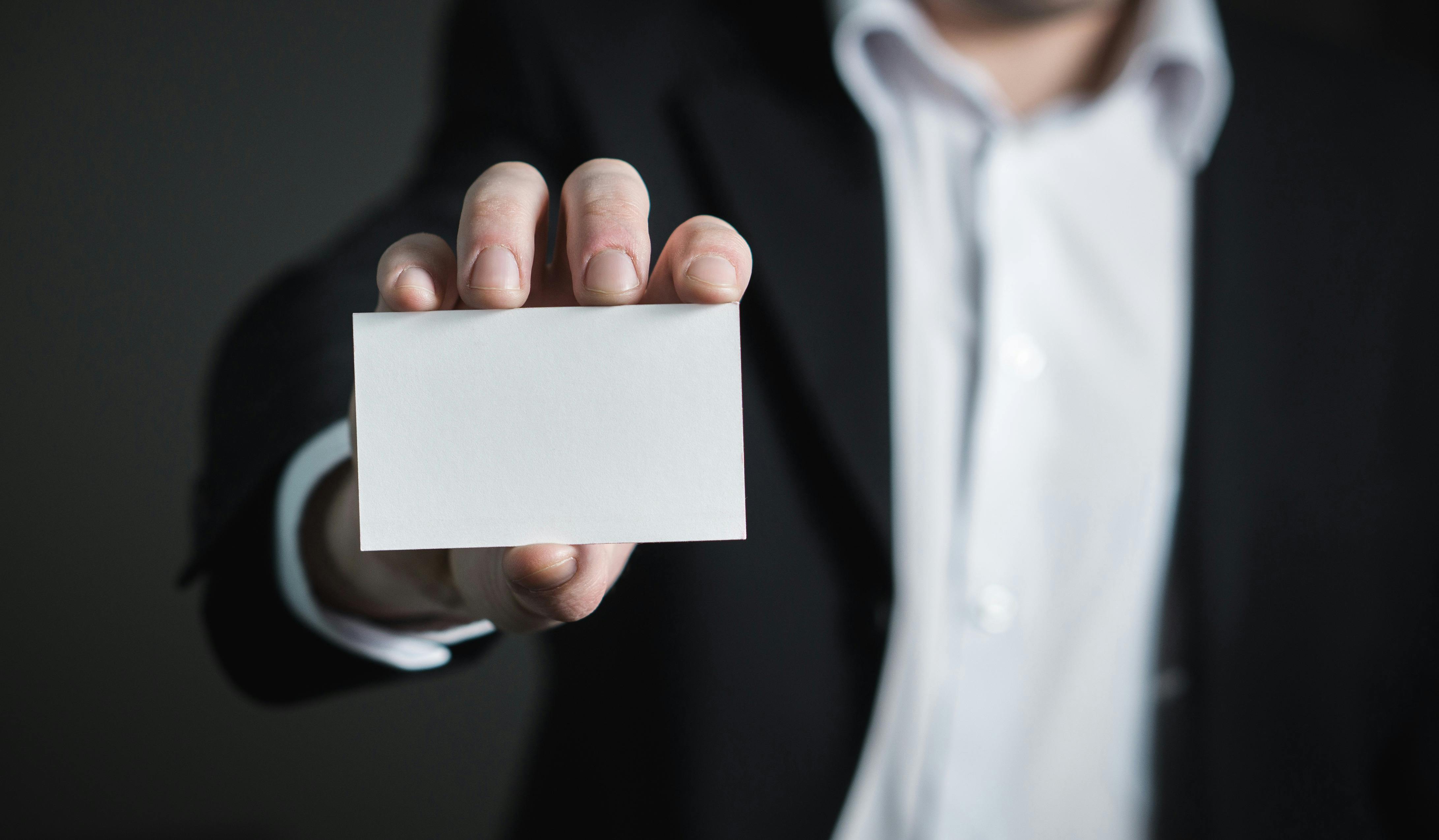 A person in a business suit holding out a blank white business card.