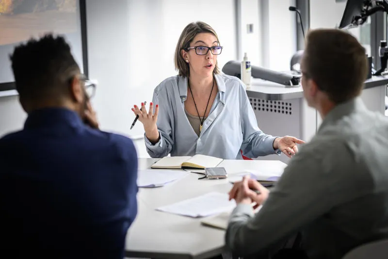 A woman with glasses speaking to 2 people from behind a desk AI in Management: Transforming Leadership for the Digital Age