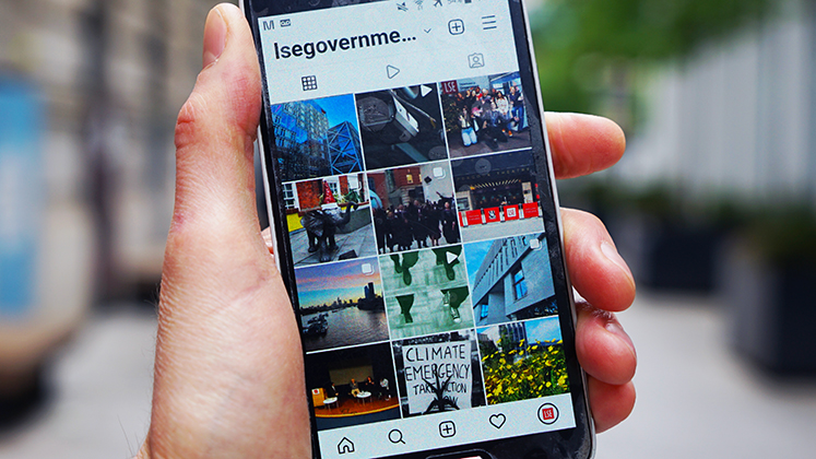 Close up photo of someone's hand holding a smartphone and looking at the LSE Government Instagram page