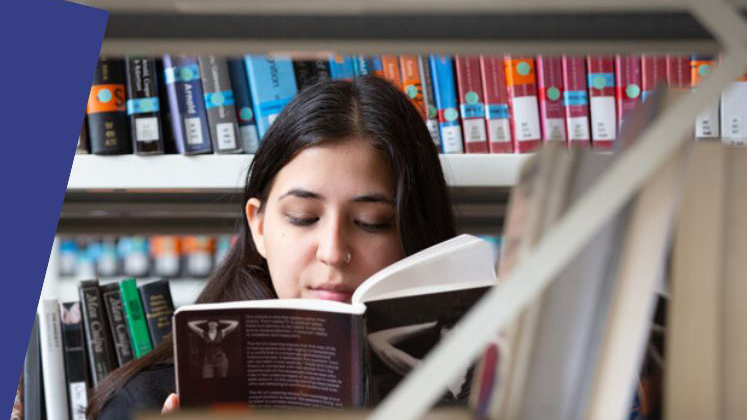 A student reading a book amongst the library shelves