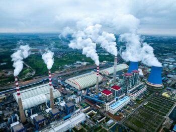 Large industrial plant with several chimneys emitting smoke, taken from above
