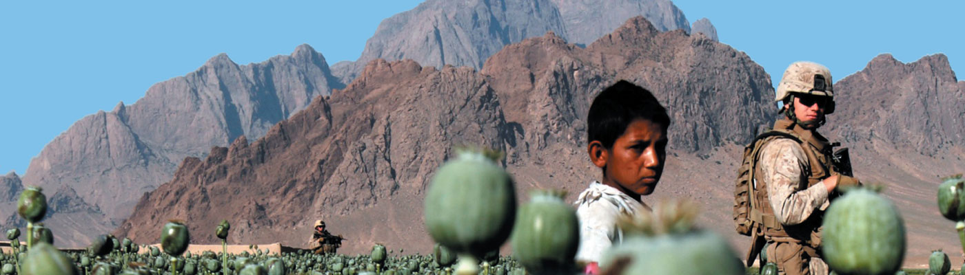 US solider and Afghan boy stand in poppy field in Afghanistan