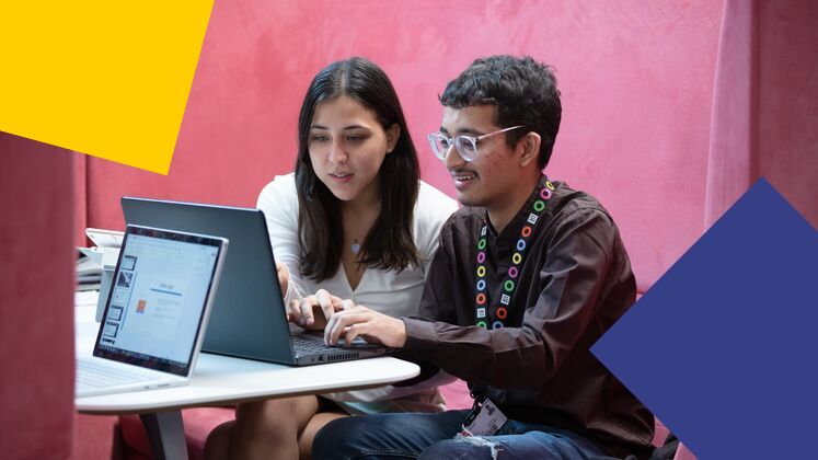 two students looking at laptop, pink wall