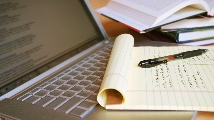 Laptop computer with books, pen and yellow legal pad 16-9 747x420