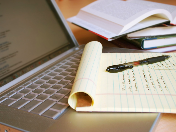 Laptop computer with books, pen and yellow legal pad 4-3 747x560