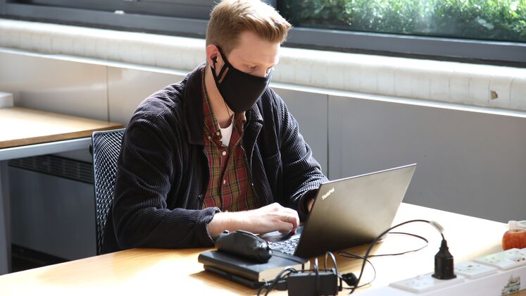 Student wearing a mask sat at a desk using a computer
