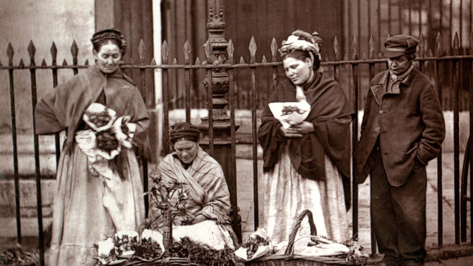 Four people in a line looking downwards at baskets in front of them which appear to have flowers in them.