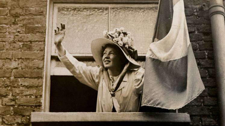 Christabel Pankhurst waving from the window of a building, and holding a flag.