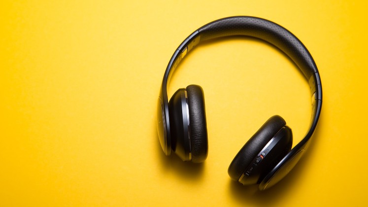 A pair of black wireless headphones on a yellow background.