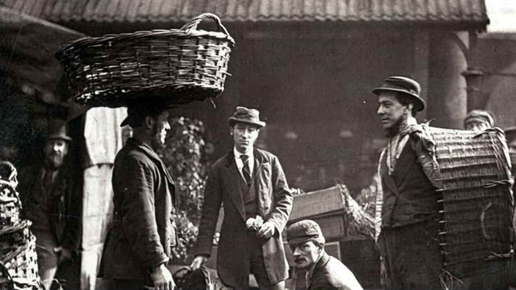 A group of labourers in Victorian London. Some appear to be carrying baskets with one of the labourers carrying a basket on their head.