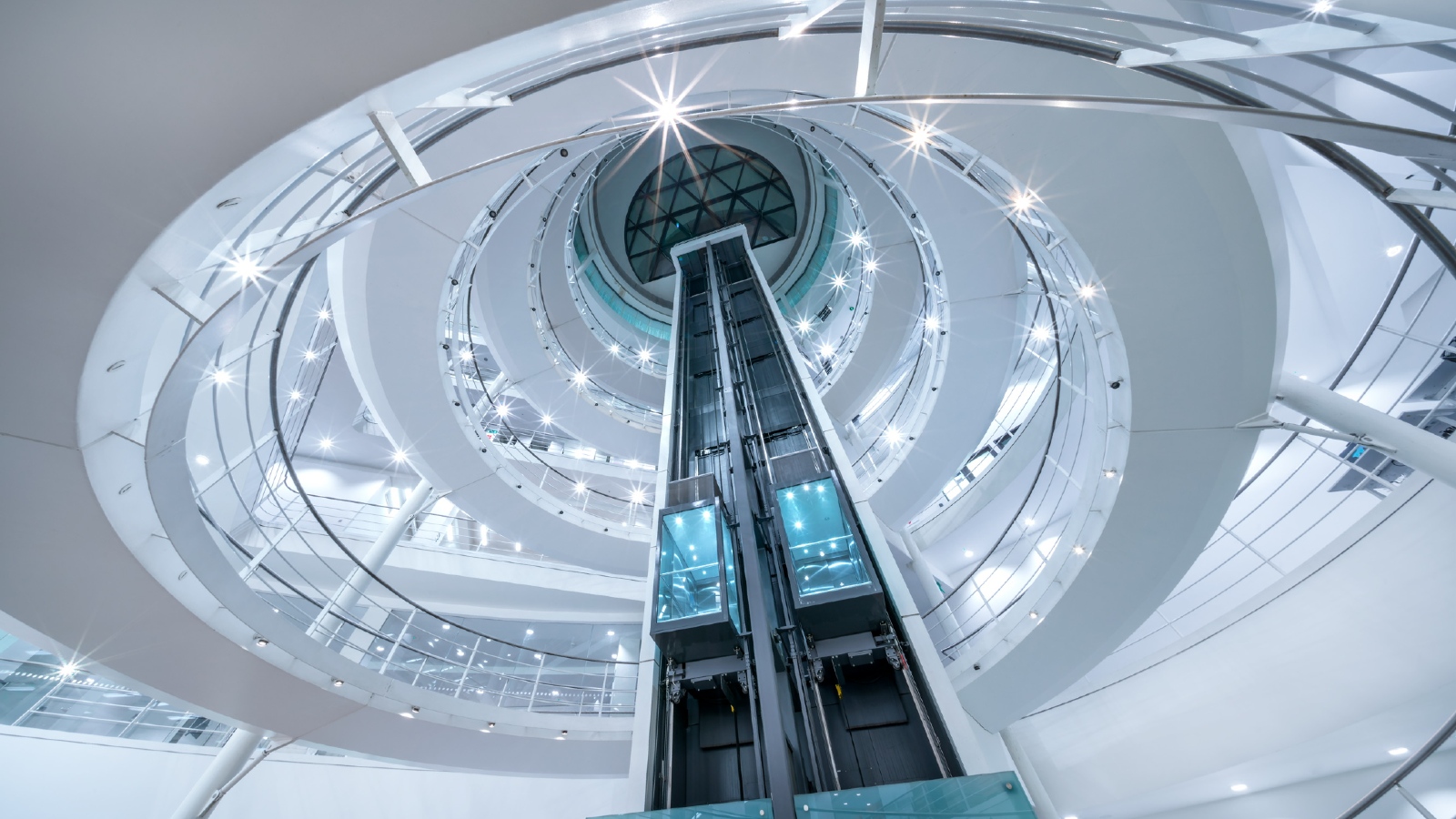 A view from inside the Library on the lower ground floor looking upwards through the void to the dome at the top of the building. It includes the the two lifts and the spiral staircase which is illuminated with lights.