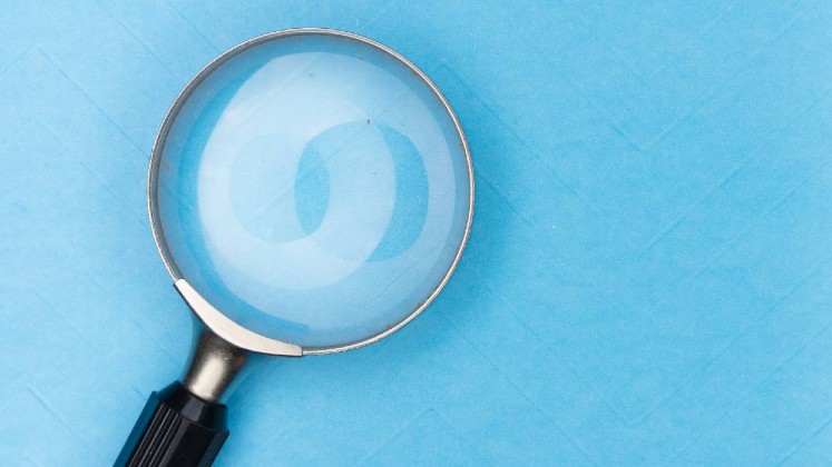 A photograph of a magnifying glass on a bright blue background.