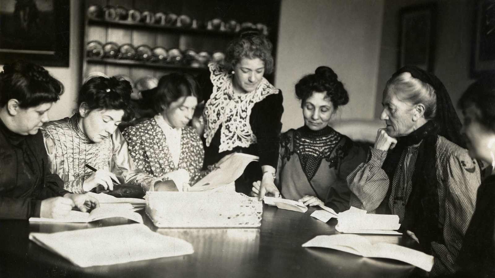 A group of women who represent the Women's Social and Political Union leadership mostly seated around a table working together.