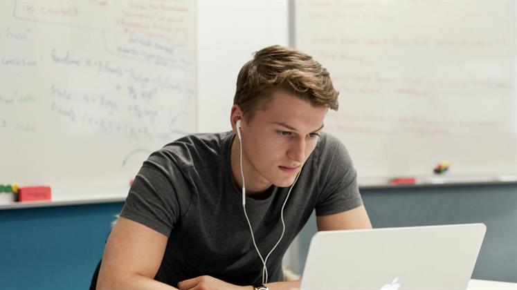 A student sitting down working at a laptop.