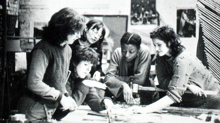 A group of 5 women working on and discussing something related to design.