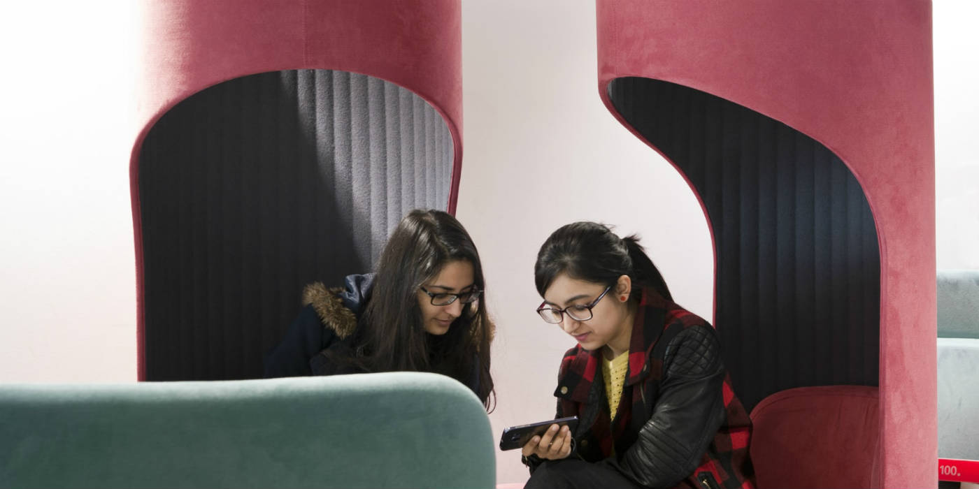 Two women sat together in the Library and looking at a phone.