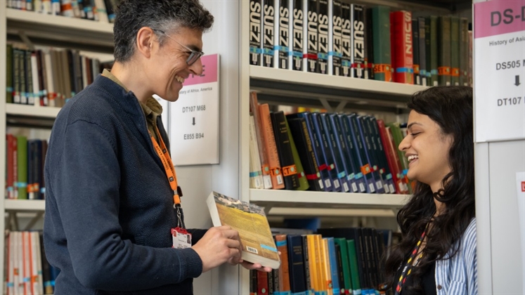 A person in the book stacks reaching up for a book