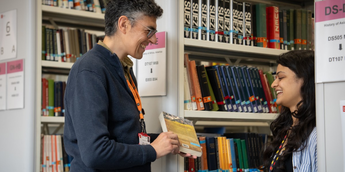 A person in the book stacks reaching up for a book