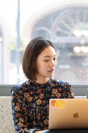 Two students sat at laptops talking to each other