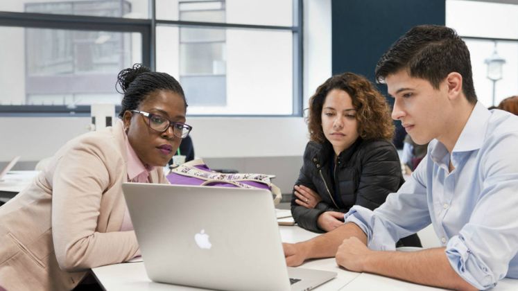 Three students sat together looking at a laptop