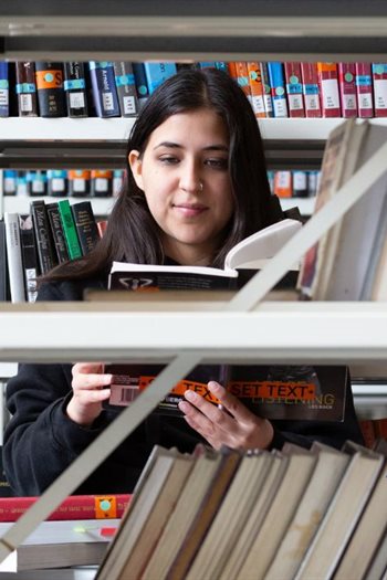 A student reading a book in the stacks