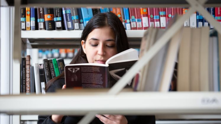 A student reading a book in the stacks