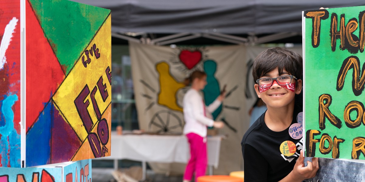 A child smiling and peering around a colourful piece of artwork for the camera.