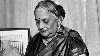 A women in Indian dress looking downwards. There is a picture of a person in a frame behind her.