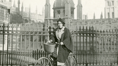 A person in university clothing riding a bike in Oxford