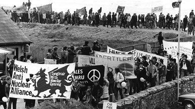 A anti nuclear march in Wales. A long line of people marching in a coastal setting with various banners.